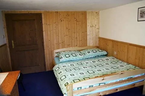 Pokoj s manželskou postelí a dřevěným obkladem stěn